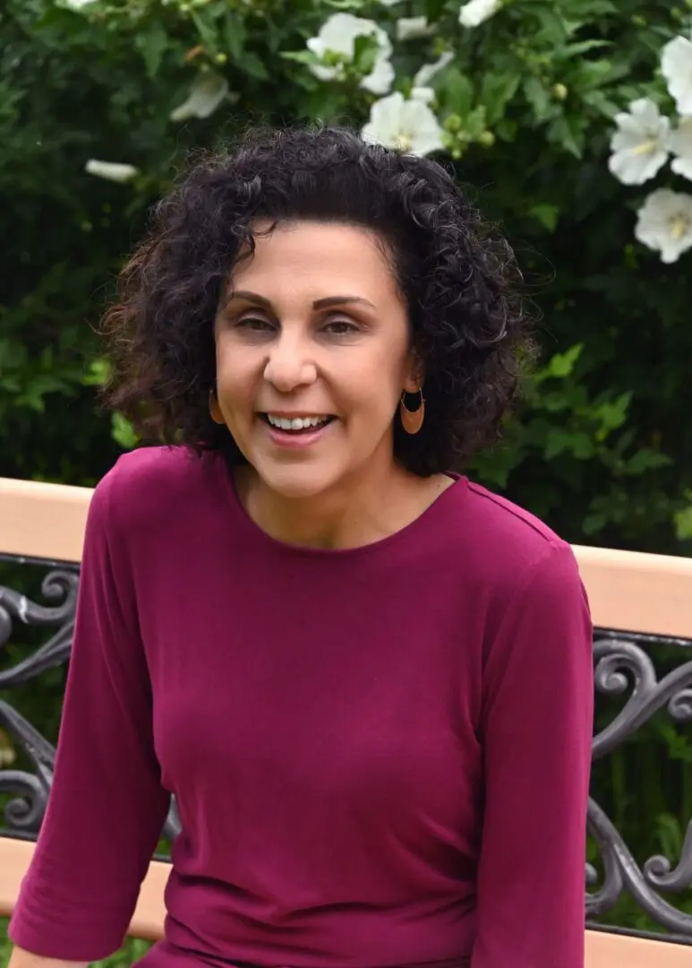 A woman in a red shirt standing next to a fence.